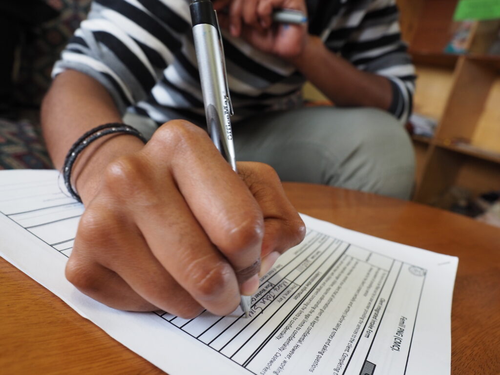 A photo of a caseworker using a pen to complete a paper form on a table. Her hand is focused with the rest of her body out of focus. 